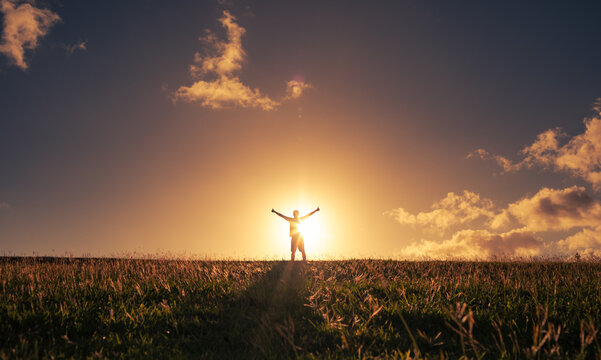 Happy state of mind. Silhouette of a person in a field with hands up to the sunlight. 