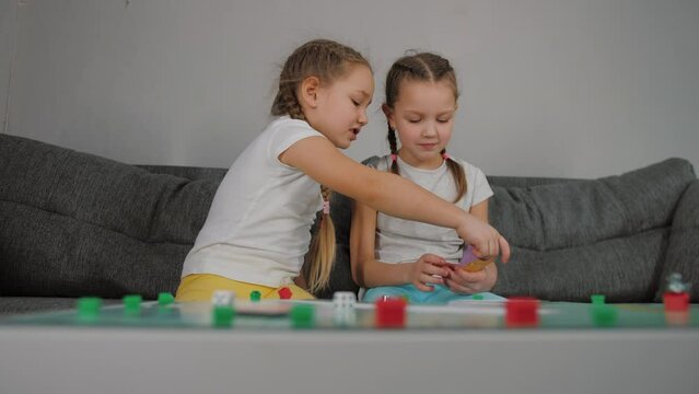 Two little girls playing tabletop game, count toy money, discuss and argue, smiles and happy. Sisters enjoy interesting board game, leisure concept