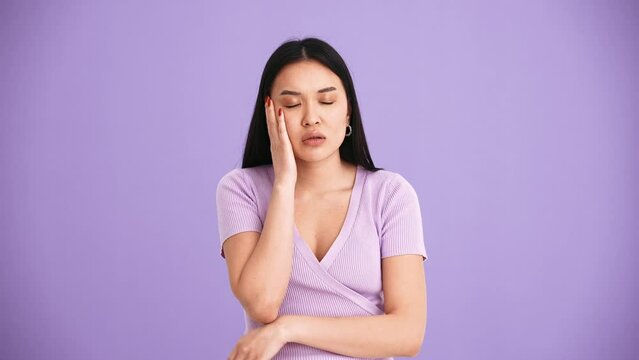 Tired Asian brunette woman wearing purple t-shirt yawning at the camera in the purple studio