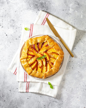 French galette or pie with peaches and in a white plate on a light gray culinary background top view. Summer homemade sweet pastries	