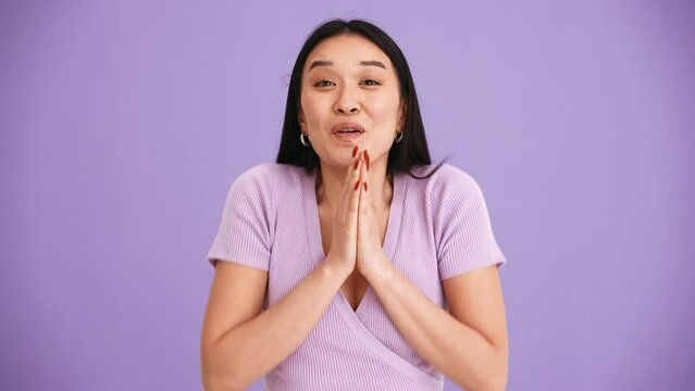 Surprised Asian brunette woman wearing purple t-shirt clapping hands at the camera in the purple studio