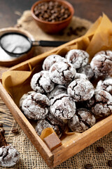 Homemade chocolate and coffee crinkle cookies in a wooden box on the kitchen table. Traditional American cookies for Christmas with cracks and powdered sugar on a dark background closeup