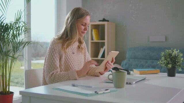 Beautiful woman chatting and browsing on her smart phone tablet while sitting on desh at her living room