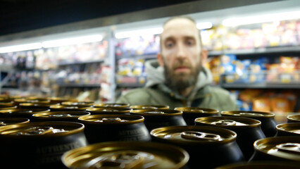 Close-up of many beautiful golden black cans of beer on a store shelf and a man standing close and choosing