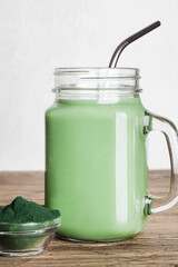 fresh green smoothie in glass bottle and spirulina powder with spoon on wooden background. useful habits, self care and healthy lifestyle. copy space