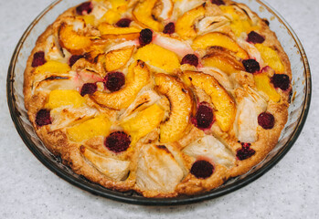 Delicious, fresh, baked apple, peach, raspberry pie close-up in a round glass form.