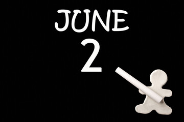 2nd day of June. A small white plasticine man writing the date 2 June on a black board. Business concept. Education concept. Summer month, day of the year concept.