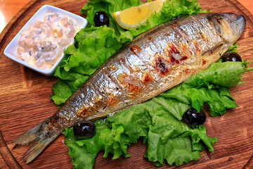 Grilled fried herring, with sauce and lemon, on a lettuce leaf, on a wooden background