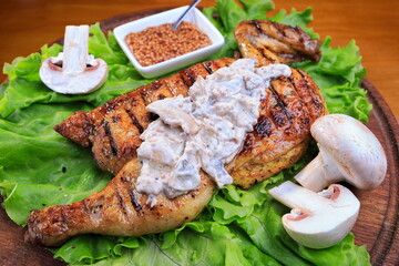 Grilled chicken half, with mushroom sauce, on a wooden background