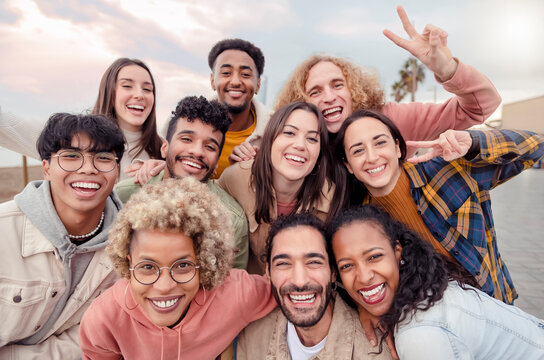 Many beautiful people standing in a circle smile at the camera taking a portrait outdoors - Large group of multiracial friends taking a selfie - Happy young students taking a photo outside school.