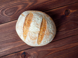 Close-up of a round loaf of wheat bread lying on a brown wooden background. Baking, bakery concept. Top view, flat lay