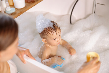 Young mom bathing her kid in large tub.