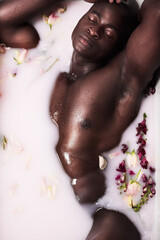 Naklejka premium You cant beat the relaxing power of a bath. Shot of a muscular young man having a milky bath filled with flowers at home.