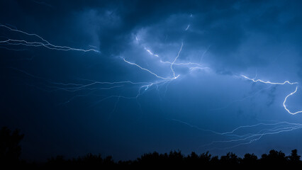 Electrical discharges during a summer storm, branched lightning bolts in the night sky.