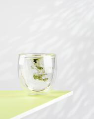 Glass of water with liquid chlorophyll on a green table. Concept of superfood, healthy eating, detox and diet. Natural light, white background, vertical. Copy space