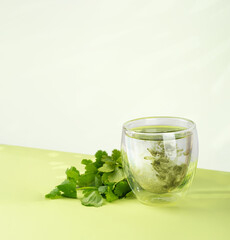 Glass of water with liquid chlorophyll and fresh herbs on a green table. Concept of superfood, healthy eating, detox and diet. Green background, copy space. Isometric