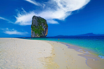 Isolated limestone rock in blue Andaman Sea lagoon, empty white sand beach, clear blue sky with...