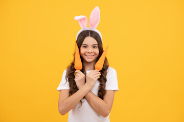 smiling kid in bunny ears hold carrot on yellow background, easter