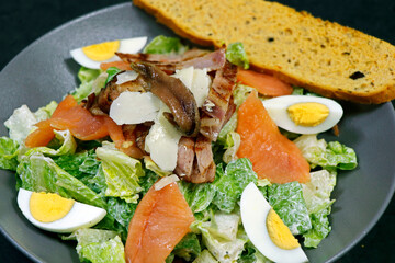 traditional caesar salad with lettuce, bread crouton, smoked salmon, eggs, anchovy and parmesan cheese in a bowl