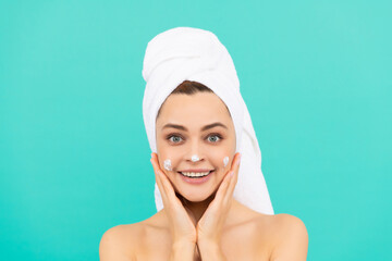 happy young girl applying face cream on blue background