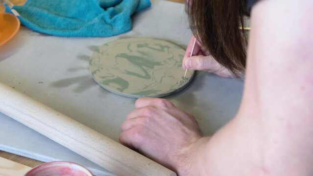A potter makes an inscription or drawing on a wet clay plate.