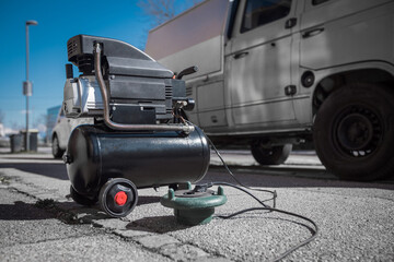 Small hobby air compressor used to pump tires or other inflatable dings, resting on a sidewalk of a town road. ready to pump an SUV tire.