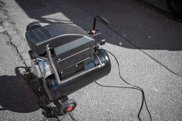 Small hobby air compressor used to pump tires or other inflatable dings, resting on a sidewalk of a...