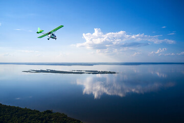A full-flowing flat river with forested banks. There is a small island in the middle of the river. The white cloud is beautifully reflected in the water. Shooting from a drone.