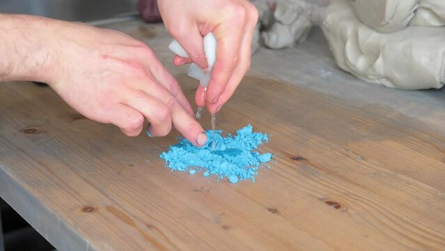 A man adds water to powdered dye. The master breeds paint on a wooden table