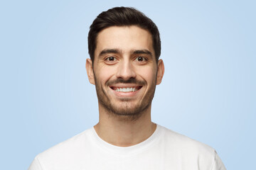 Young smiling handsome man in white t-shirt stands isolated on blue background