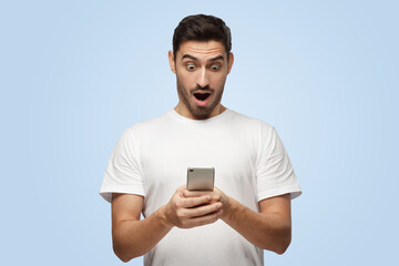 Attractive young man looks agitated at smartphone impressed by web content