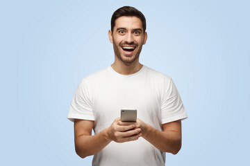 Cheerful young man in t-shirt holds smartphone looking at camera and laughing