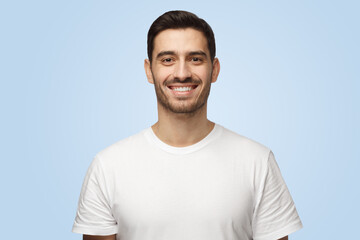 Smiling attractive handsome man in t-shirt looks at camera isolated on blue background