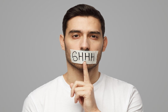 Young man with shhh gesture and taped mouth, asking for silence or to be quiet