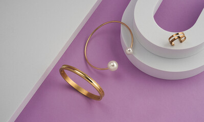Top view of golden with pearls bracelet and ring on white podium on purple background