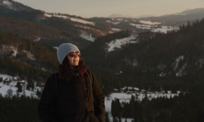 Smiling woman wearing hat and sunglasses enjoying the views of snowy Carpathian mountains in Ukraine