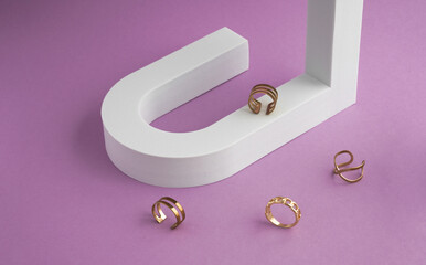 Modern golden rings collection on white u shape podium and purple background with copy space