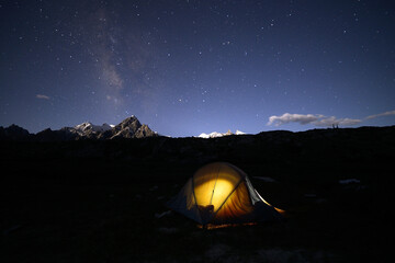 Een vaag Melkwegstelsel en verlichtte een kamp van trekkers op de rand van de Biafo-gletsjer, Karakoram Range, Pakistan.