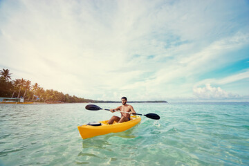 Young strong man kayaking in the sea near the tropical island. Adventure by kayak.