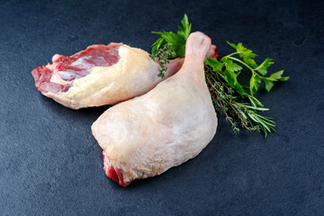 Traditional raw gourmet duck leg offered with herbs as close-up on a black design board