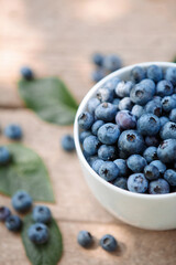 A bowl with fresh bilberry (Vaccinium myrtillus) on an old wooden bench. Fresh garden blueberries.