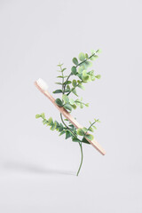 Minimal sustainable beauty, fashion and lifestyle concept with wooden toothbrush and green leaves on gray background. Environmental protection, health and sustainability idea. Eco friendly aesthetics.