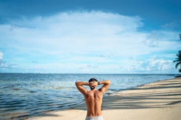 Holiday on the beach. Back view of relaxed young muscular man enjoying sea view.