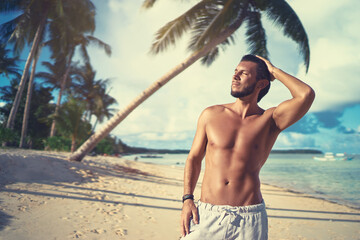 Enjoying suntan and vacation. Portrait of young bearded man on the tropical sand beach.