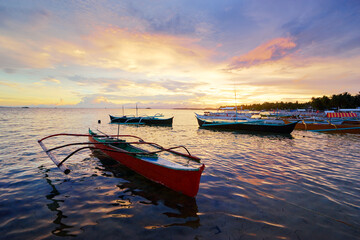 Naklejka na ściany i meble Beautiful colorful sunset on the seashore with fishing boats. Philippines, Siargao Island.