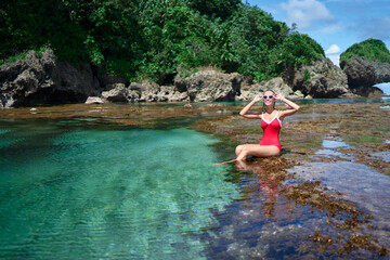 Summer vacation. Young woman in red swimsuit bathing at sea natural pool.
