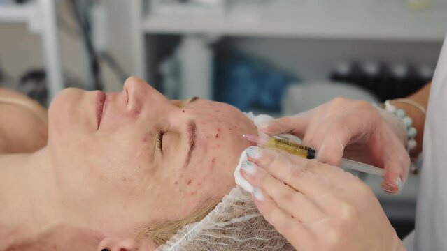 Cosmetologist making botox injection to forehead of middle-aged woman in clinic. Crop view of beautician injecting face lifting for female patient with closed eyes in salon. Concept of beauty care