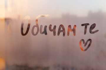 Lettering text in Bulgarian language words I love you in english and heart shape on sunset wet window