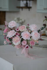 Beautiful bouquet of peonies and pink roses on the table. In the background is the interior of a modern white kitchen. Concept of home comfort.