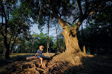 Vacation concept. Happy young woman in hat sitting in swing.